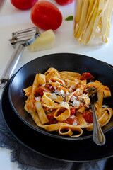 Italian lunch. Neapolitan pasta. Italian pasta dish with tomatoes, basil, onions. Black plate.