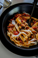 Italian lunch. Neapolitan pasta. Italian pasta dish with tomatoes, basil, onions. Black plate.