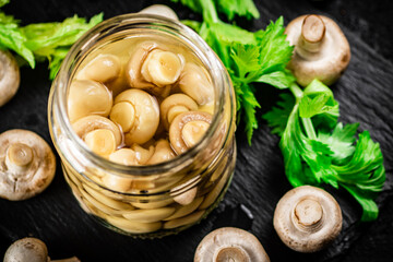 Pickled mushrooms in a jar with greens on a stone board. 