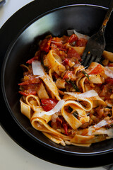 Italian lunch. Neapolitan pasta. Italian pasta dish with tomatoes, basil, onions. Black plate.