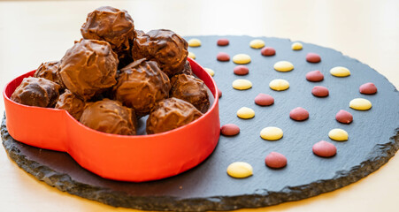 Chocolate pralines in a red heart box and chocolate flakes on a slate plate