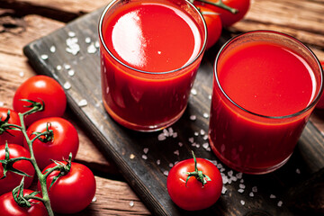Glasses with tomato juice on a wooden cutting board. 