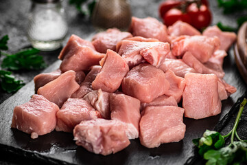 Pieces of raw pork on a stone board with parsley, tomatoes and spices. 