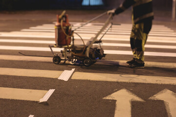 Process of making new road surface markings with line striping machine, workers improve city infrastructure, demarcation marking of pedestrian crossing with hot melted paint on asphalt pavement