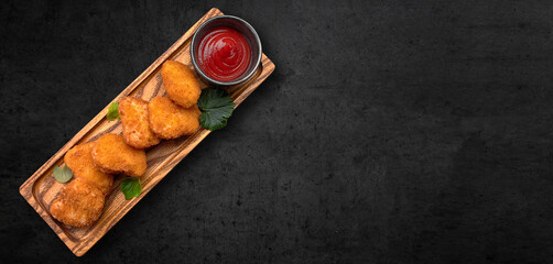 Fried chicken nuggets with ketchup, on a wooden board. Banner