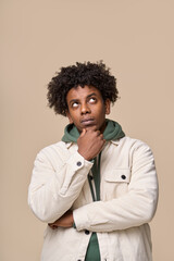 Fototapeta na wymiar Young thoughtful doubtful African American guy student thinking of idea holding hand on chin, looking up choosing, making decision, feeling doubt having question isolated on beige background. Vertical