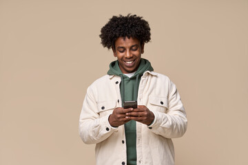 Young happy cool curly African American ethnic gen z guy holding cell phone, smiling teen using mobile digital apps on cellphone technology texting on smartphone isolated on light beige background. - obrazy, fototapety, plakaty