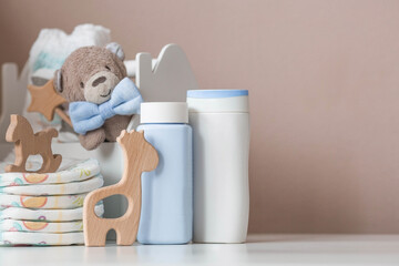 Wooden toys, a bear in a bow tie, a stack of diapers, bottles without labels and baby supplies on the changing table. Space for text.