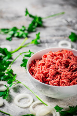 Minced meat in a bowl on a table with parsley and onion rings. 