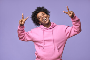 Young cheerful happy hipster African American teen guy wearing pink hoodie isolated on light purple background. Smiling cool joyful ethnic generation z teenager model laughing showing peace sign. - obrazy, fototapety, plakaty
