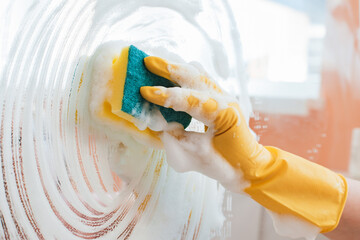 woman does household chores at home, washing the surfaces of mirrors and windows with a spray of detergent with a foam sponge.