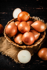 Whole onions in a basket with halves of onions on the table. 