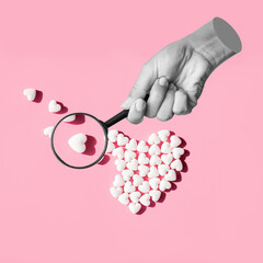 Female statue's hand holding a magnifying glass enlarging white heart-shaped tablet isolated on a...