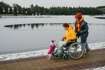 Caucasian woman driving her friend in a wheelchair along the lake in winter.