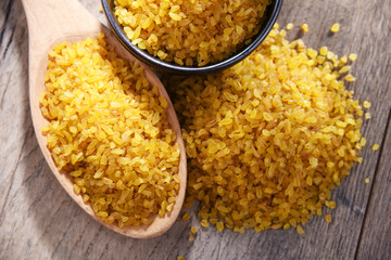 Composition with a bowl and spoon of uncooked bulgur on a table