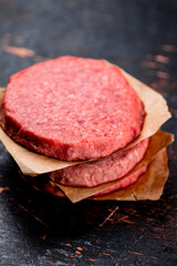 Raw burger on paper. On a rustic dark background.
