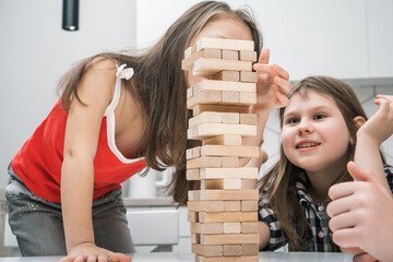 Group of enthusiastic children players playing board game Jenga on table in kitchen at home,...