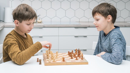 Side view of two calm focused preteen boys friends brothers sitting at white table in kitchen at...