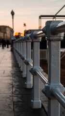 Vertical photo of Gijon city walkway white fence at golden hour with sbeach close to the walkway, placed in Asturias, Spain.