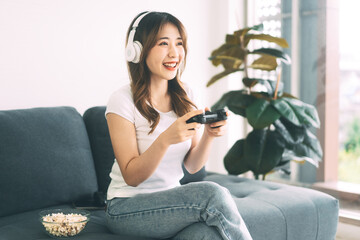 Asian woman hand holding a joy controller wear headset and play game sitting on sofa at home