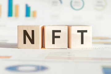 NFT abbreviation from wooden block on financial background. Modern technologies concept
