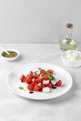 Caprese Salad with ripe tomatoes, mozzarella cheese, fresh basil, balsamic sauce, pesto on white plate. Healthy delicious diet salad.