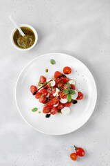 Caprese Salad with ripe tomatoes, mozzarella cheese, fresh basil, balsamic sauce, pesto on white plate. Healthy delicious diet salad.