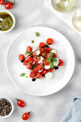 Caprese Salad with ripe tomatoes, mozzarella cheese, fresh basil, balsamic sauce, pesto on white plate. Healthy delicious diet salad.