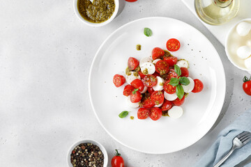 Caprese Salad with ripe tomatoes, mozzarella cheese, fresh basil, balsamic sauce, pesto on white plate. Healthy delicious diet salad.