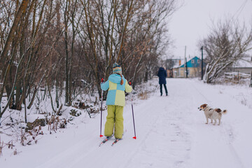 Happy child is skiing in the park. A teenager is engaged in winter sports in nature with his beloved pet. A beautiful girl walks with a dog along a winter road. Children go skiing during the holidays.