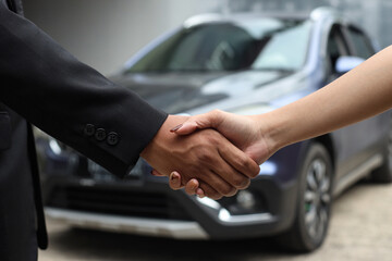 Cropped closeup image of a salesman shaking hands with his client after selling a car at the...