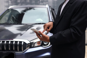 Cropped shot of car dealer sales wearing suit is using tablet in front of car. 