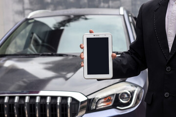 Cropped shot of car dealer sales wearing suit is holding blank screen tablet for mock up in front of car. 