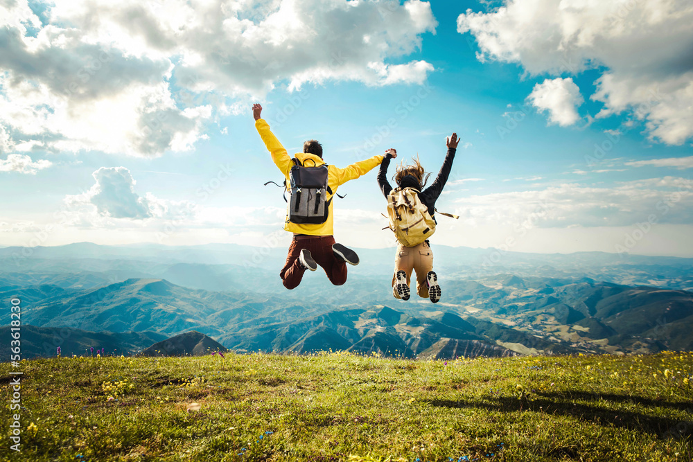 Wall mural hikers with backpack jumping with arms up on top of the mountain