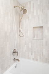 An empty shower with vertical brown subway tiles and small, a built-in shelf, with a gold shower...