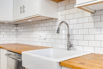 A kitchen sink detail with wood countertops, white cabinets, an apron sink, and a subway tile...