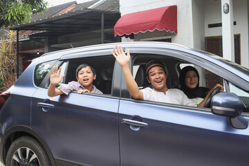 Excited muslim family are smiling and waving hand inside the car ready to go on holiday. Mudik lebaran at Eid moment. 