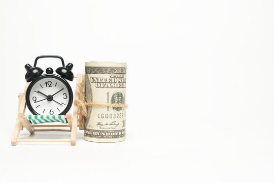 Selective focus picture roll fake money on folding beach chair and alarm clock on copyspace white background . Future financial and work life balance concept.
