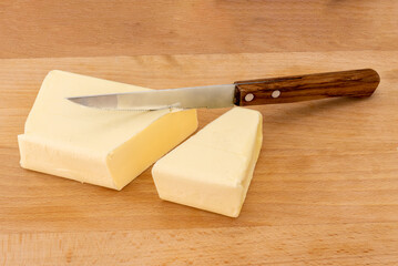 Block of butter cut with wooden handled knife on wooden cutting board