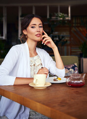 Beautiful girl sitting in restaurant, drinking red fruit tea and eating cake. Attractive smiling young woman in cafe. Indoor portrait of cute lady