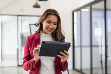 Young attractive female manager working on digital tablet while standing in modern office