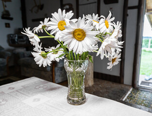 Floral bouquet in retro crystal vase on table in country interior. Wild chamomiles flowers bunch on desk in rustic style