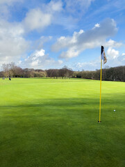 Flag and the hole at golf club blue sky summers day with some clouds.