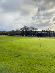 Obraz premium Flag and the hole at golf club blue sky summers day with some clouds.