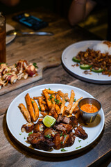 Grilled pork steak served with french fries, sliced lime, and chili sauce on the white plate. Bokeh background. Portrait or vertical.