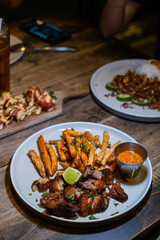 Grilled pork steak served with french fries, sliced lime, and chili sauce on the white plate. Bokeh background. Portrait or vertical.