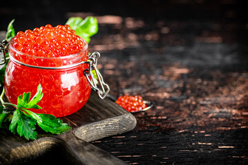 A full glass jar of red caviar on a cutting board. 