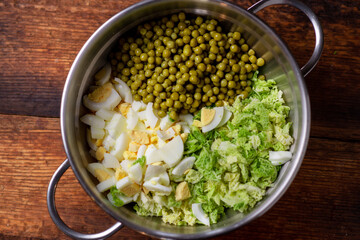 Savoy cabbage salad. The ingredients are in a saucepan - green peas, chicken eggs and cabbage. Preparing a vegetarian salad.