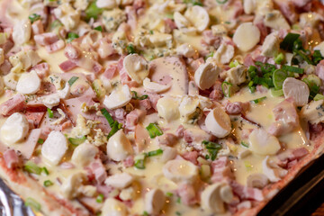 Cooking homemade pizza on a baking sheet. Pizza with mozzarella cheese, herbs and ham.