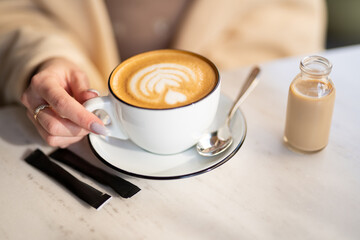 a fragrant and warm mug of cappuccino with a drawing heart,  girl  hold in hands.